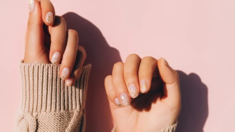 glowing hands in sweater with knitted sleeves and with nude color manicure with gold particles on pink table trendy colors of the year 1 1620x911 1 scaled 1